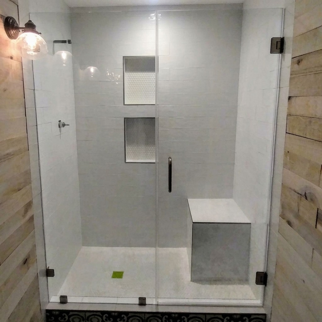 Frameless inline glass shower door and panel with black hardware and a tiled bench