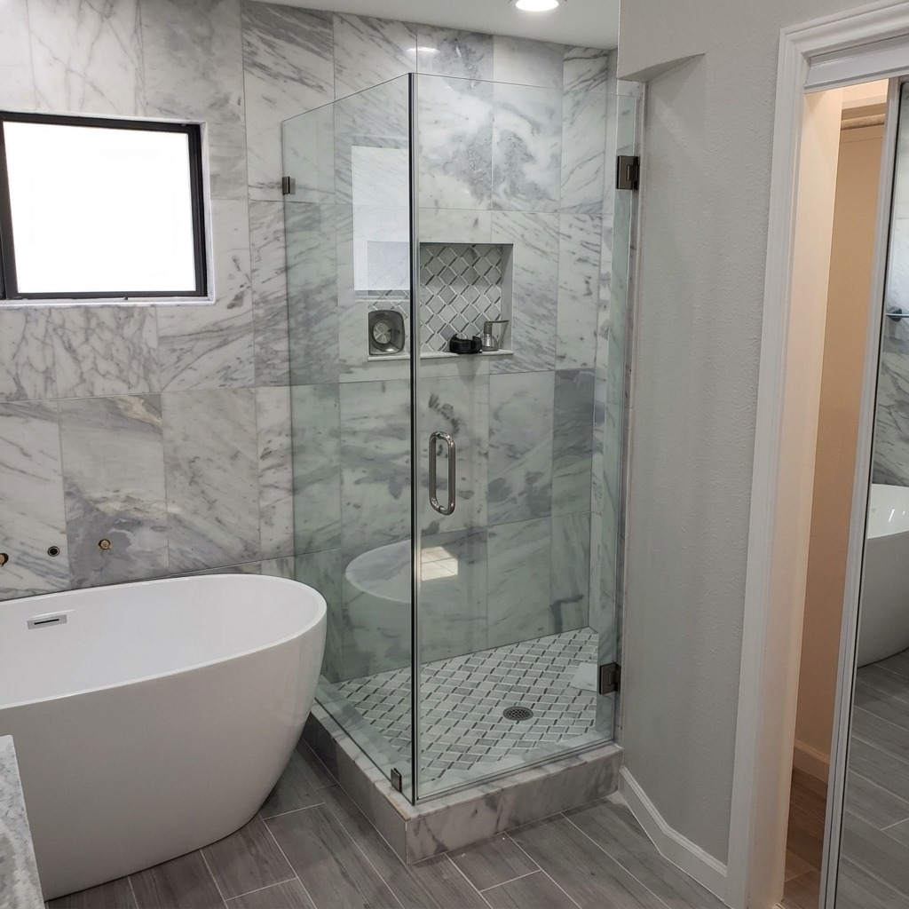 Frameless glass shower enclosure with marble tile beside a freestanding tub