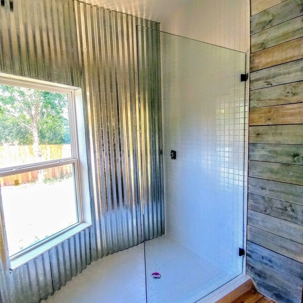 Fixed frameless glass shower panel beside a corrugated metal wall