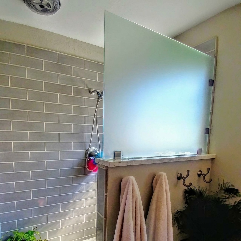 Frosted frameless glass shower panel mounted on a tiled half wall