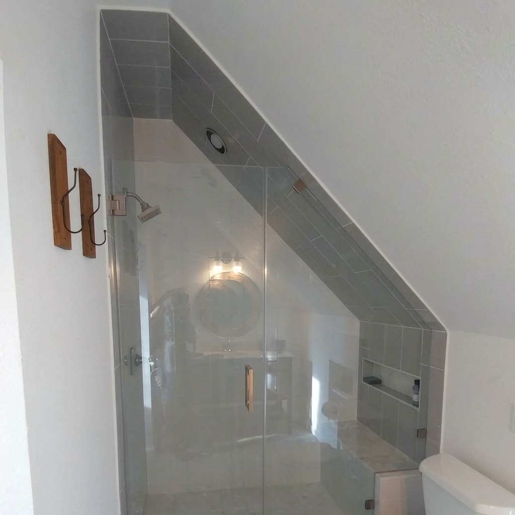 Custom raked frameless glass shower enclosure under a slanted roofline