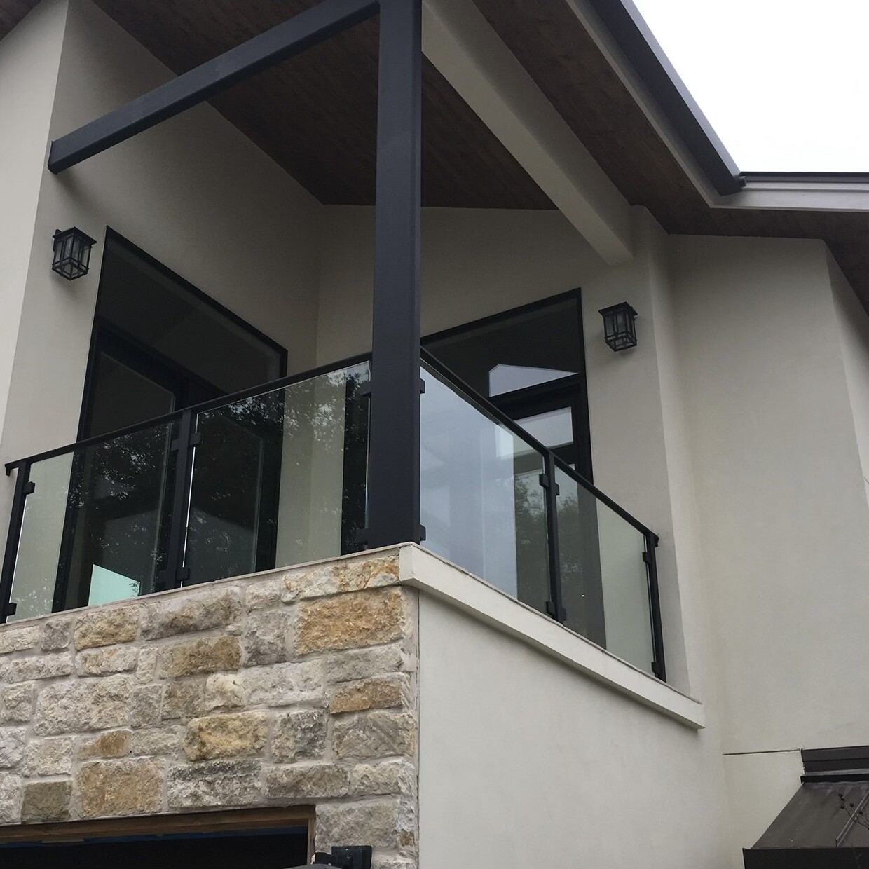 Glass balcony railing with black posts on a second-story balcony above a stone ledge