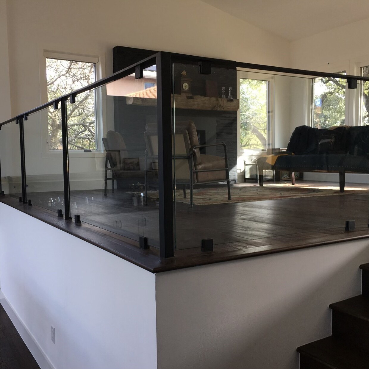 Glass railing with black posts and top rail around a raised living room platform