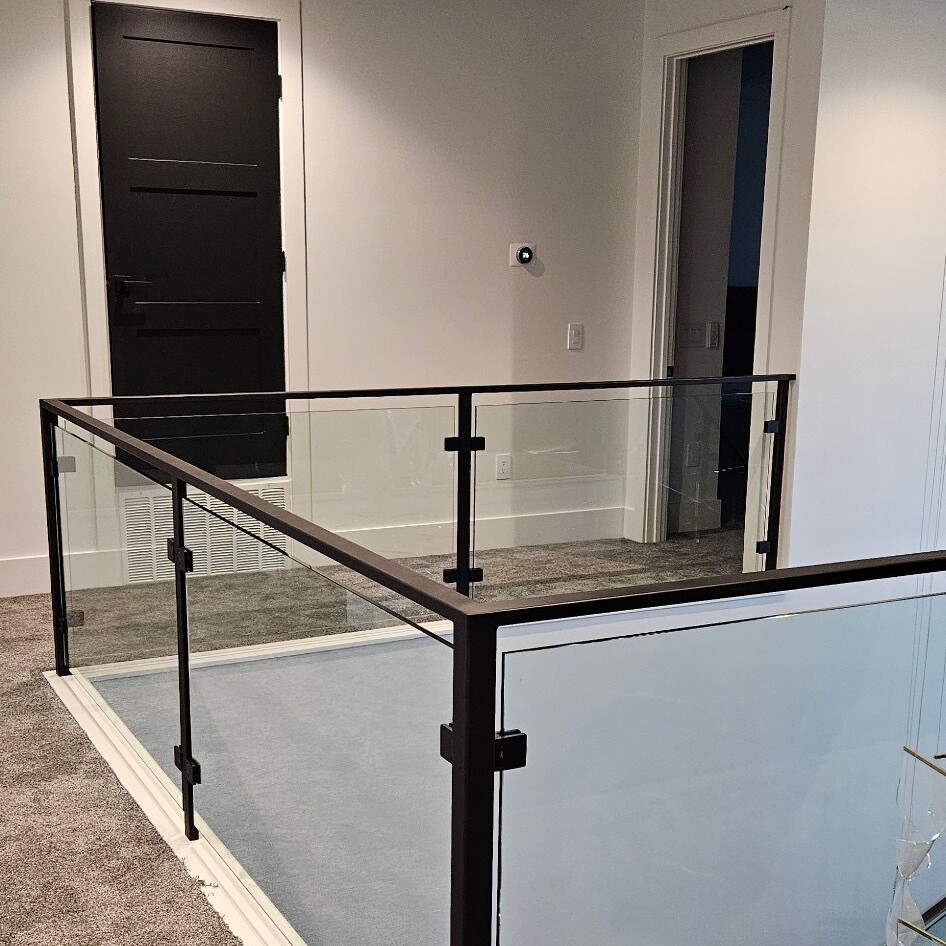 Glass railing with black posts and handrail around a carpeted upstairs stair opening