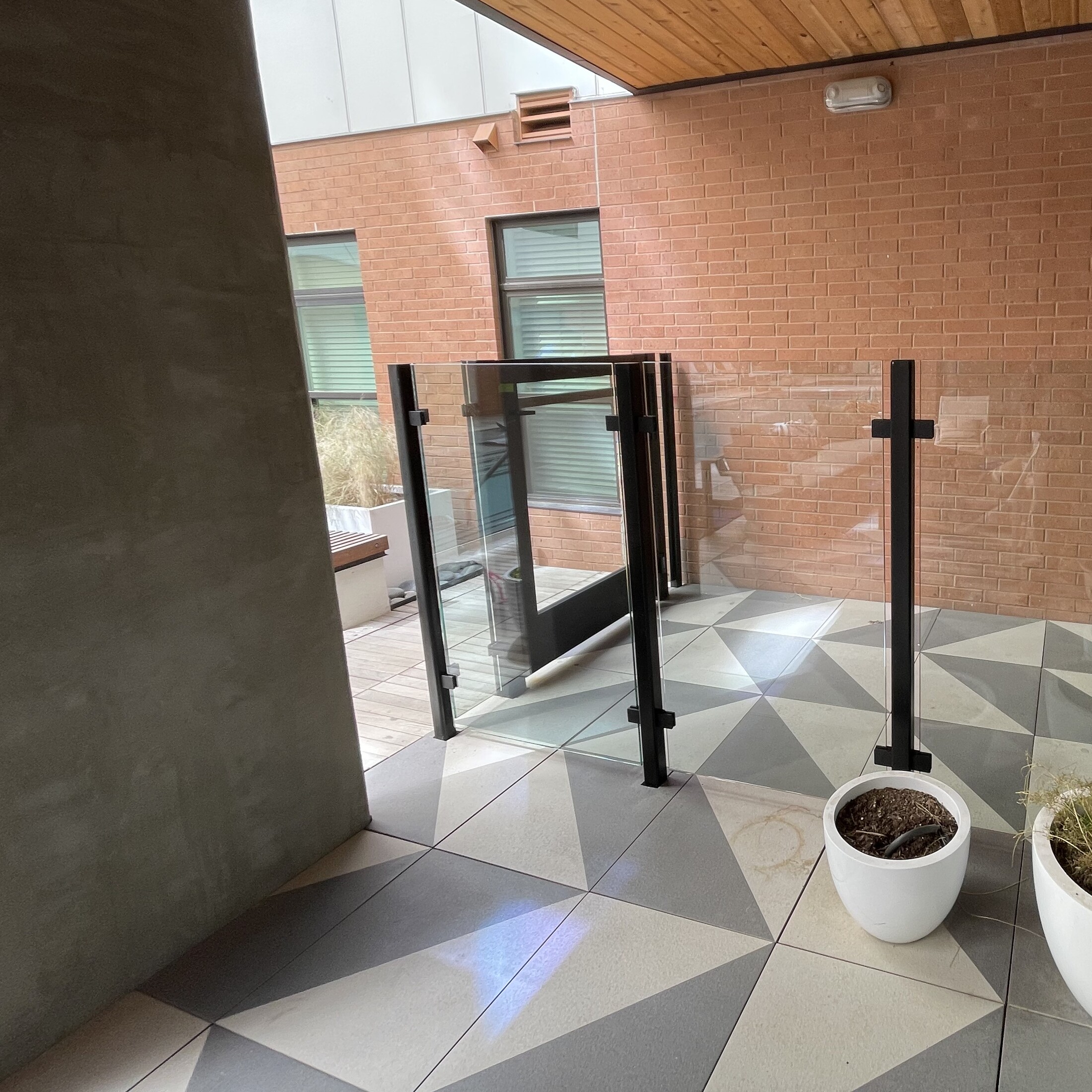 Glass patio railing with black posts and a matching glass gate on a covered tiled patio
