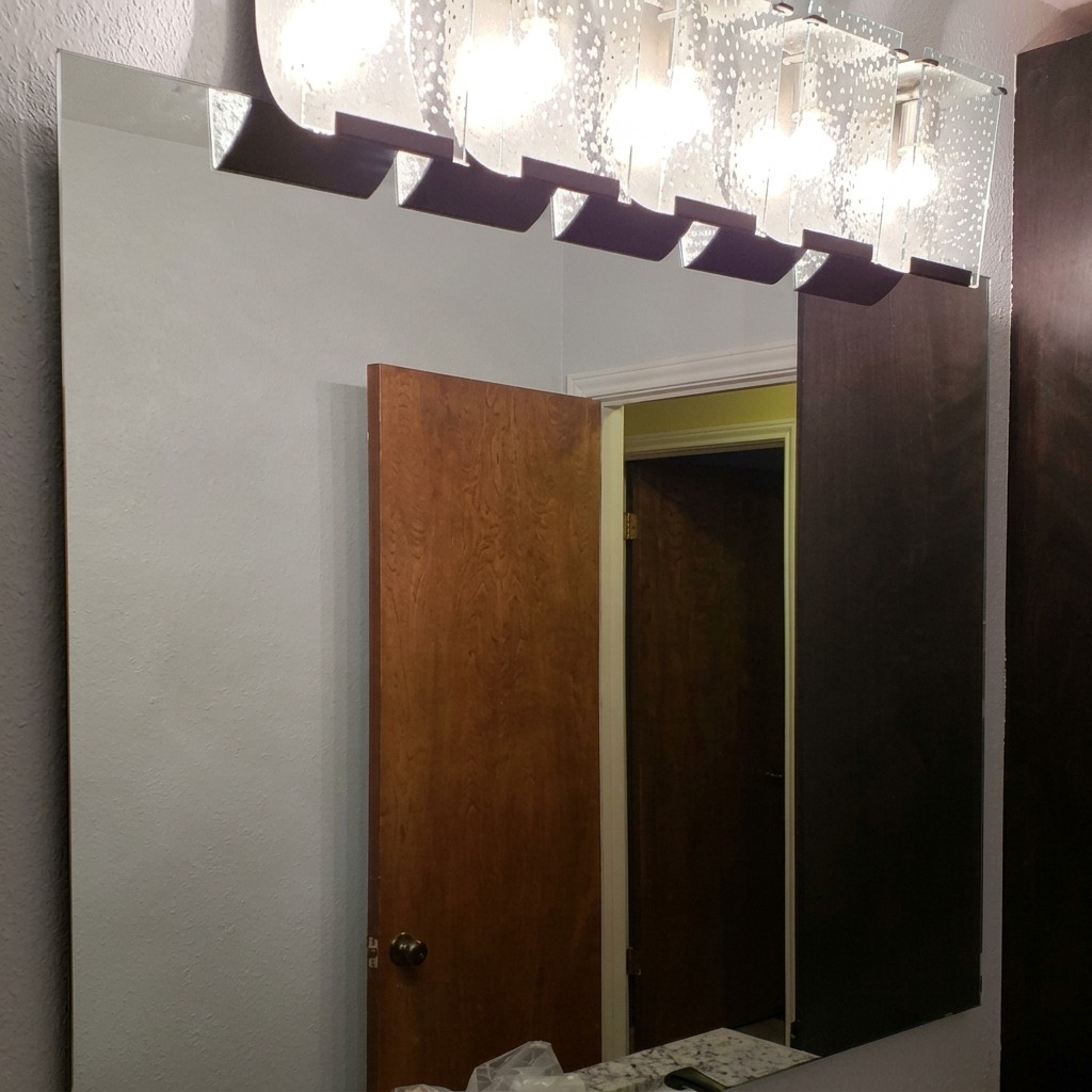 Large frameless wall mirror mounted beneath a glass vanity light bar