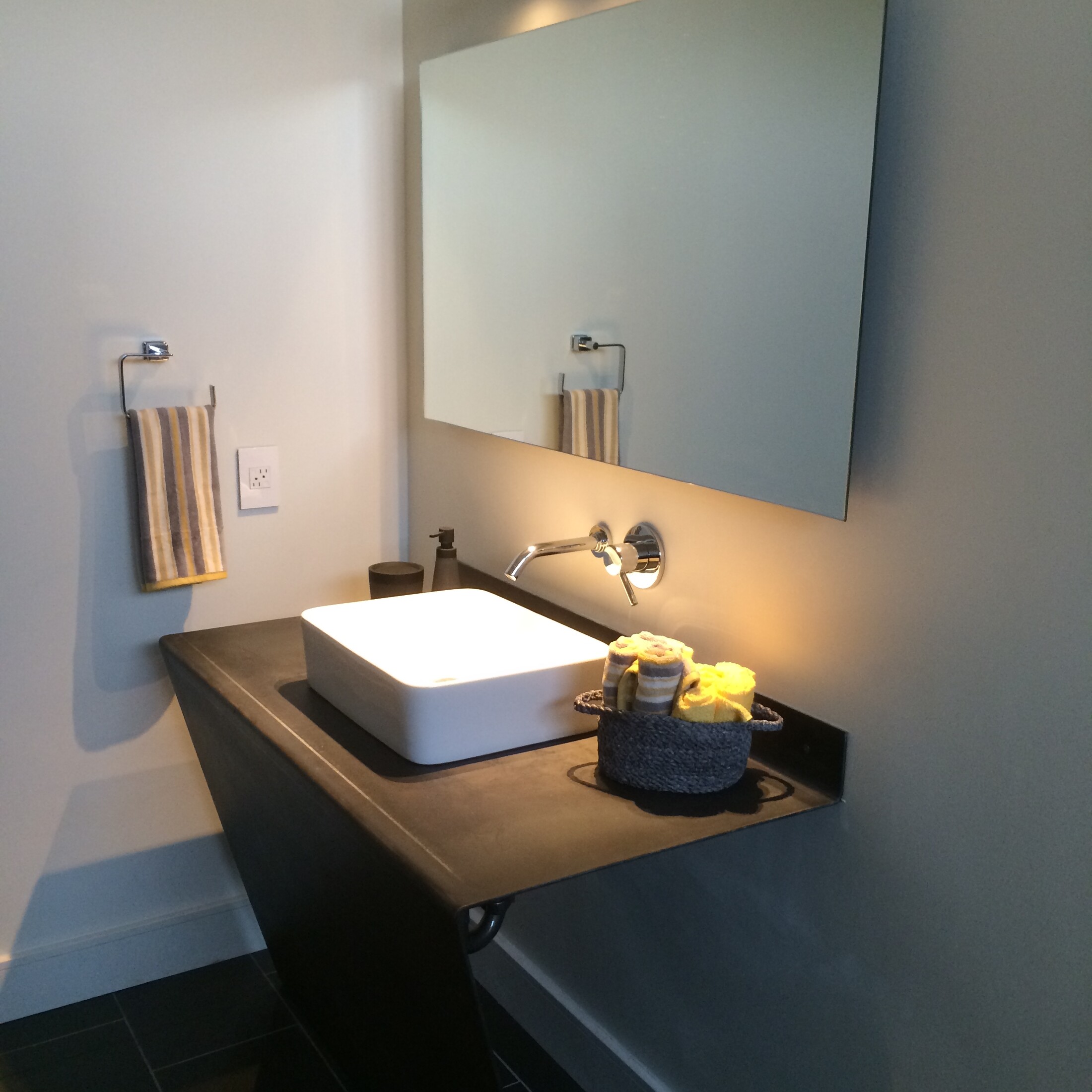 Frameless wall mirror above a dark sculpted pedestal vanity with a white vessel sink