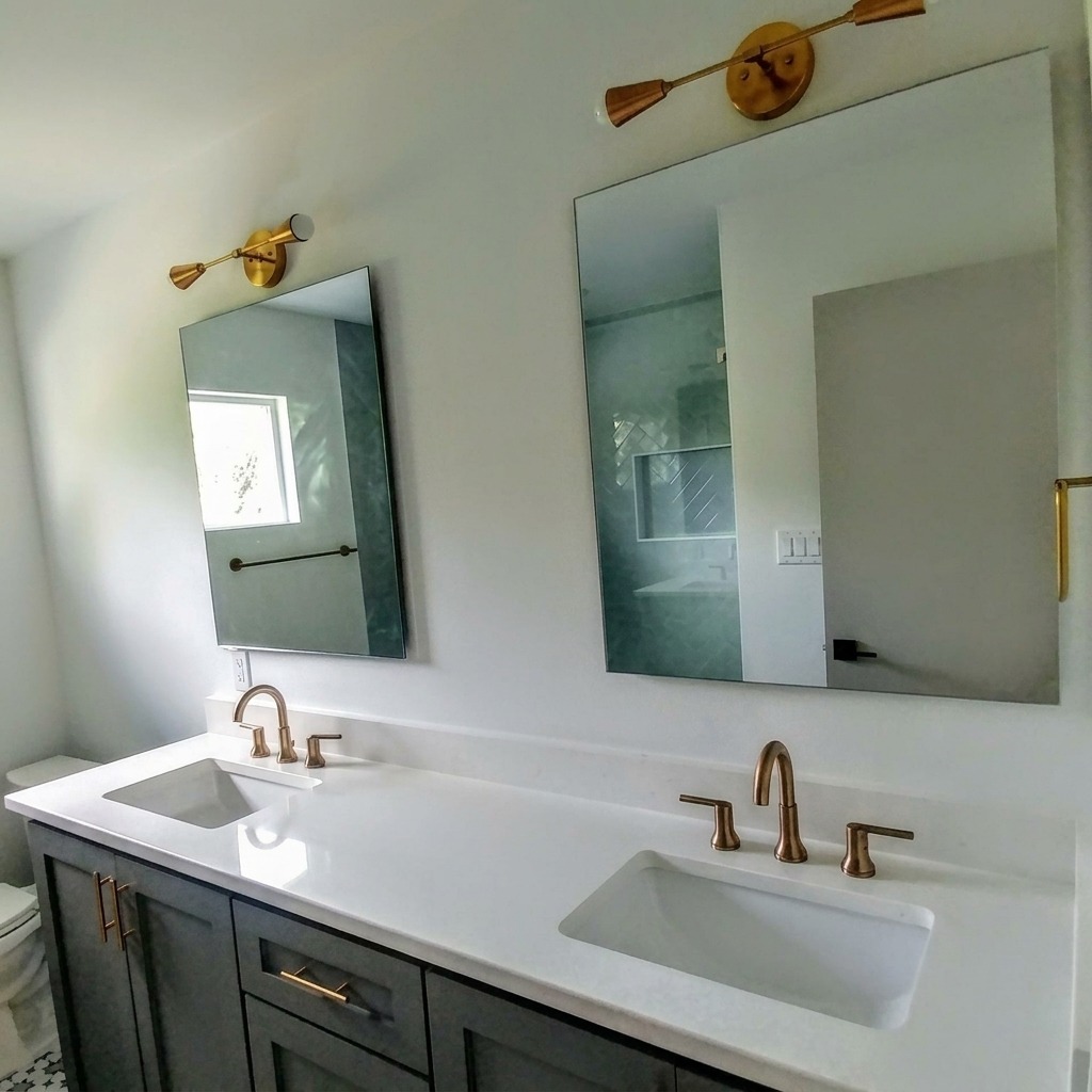 Two frameless vanity mirrors under brass sconces above a white double vanity