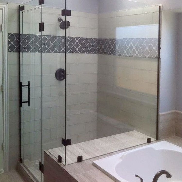 Frameless 90-degree shower enclosure with matte black hardware beside a drop-in tub