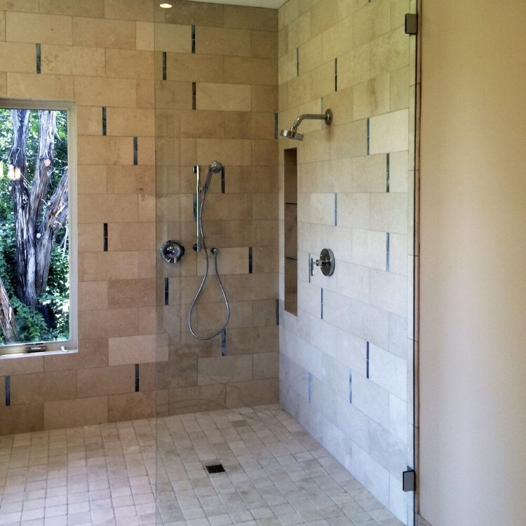 Frameless glass walk-in shower panel with stacked stone tile and a window