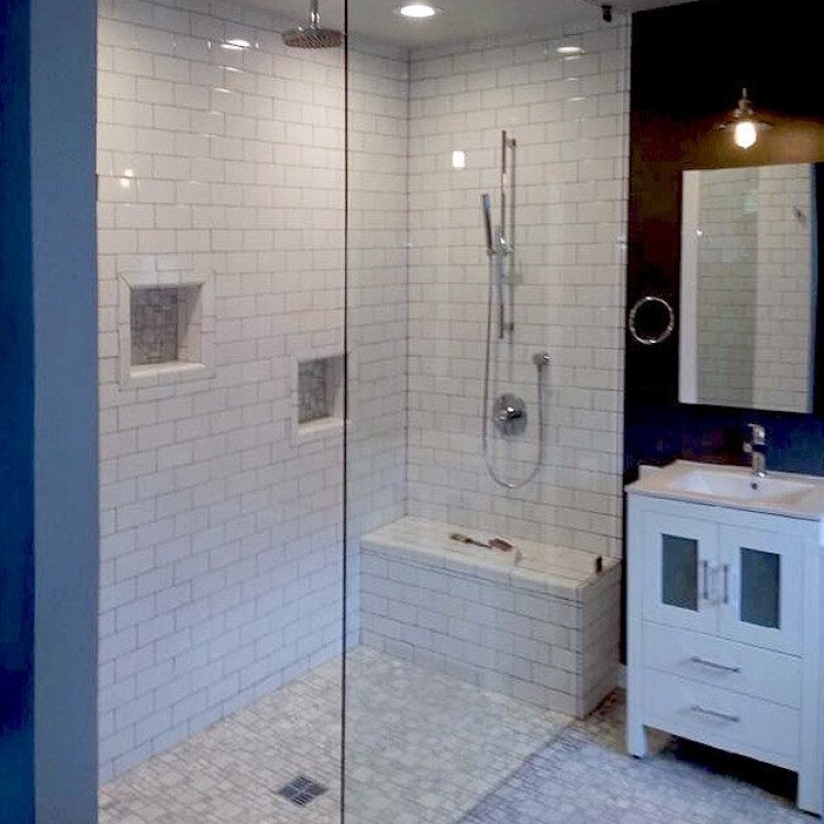 Frameless glass shower panel with white subway tile and a built-in bench