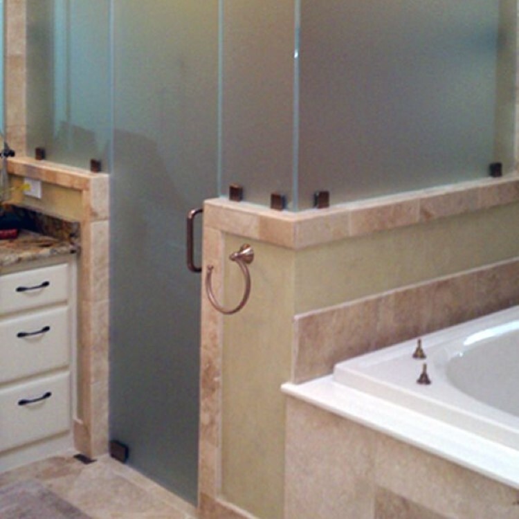 Frosted glass shower enclosure on a tiled half wall beside a tub