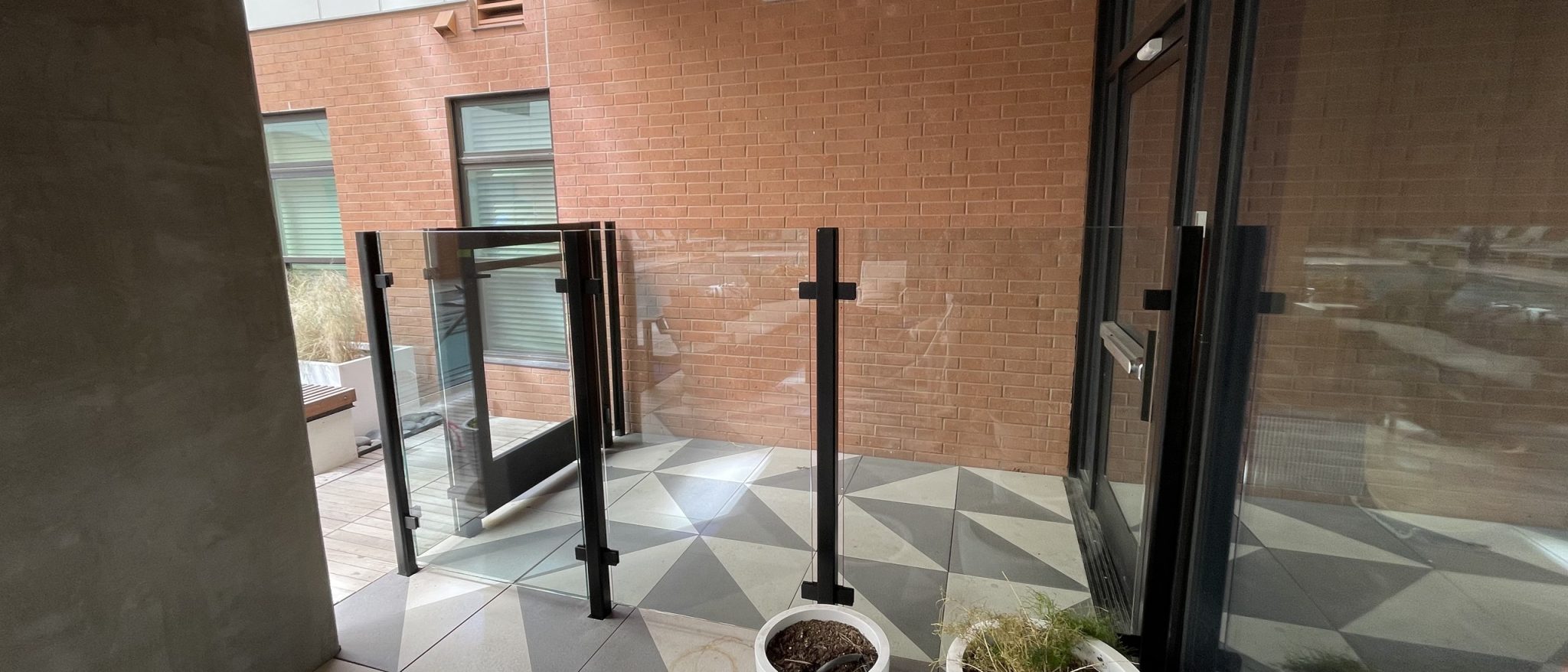 Glass railing with black posts and a matching glass gate around a patterned-tile courtyard