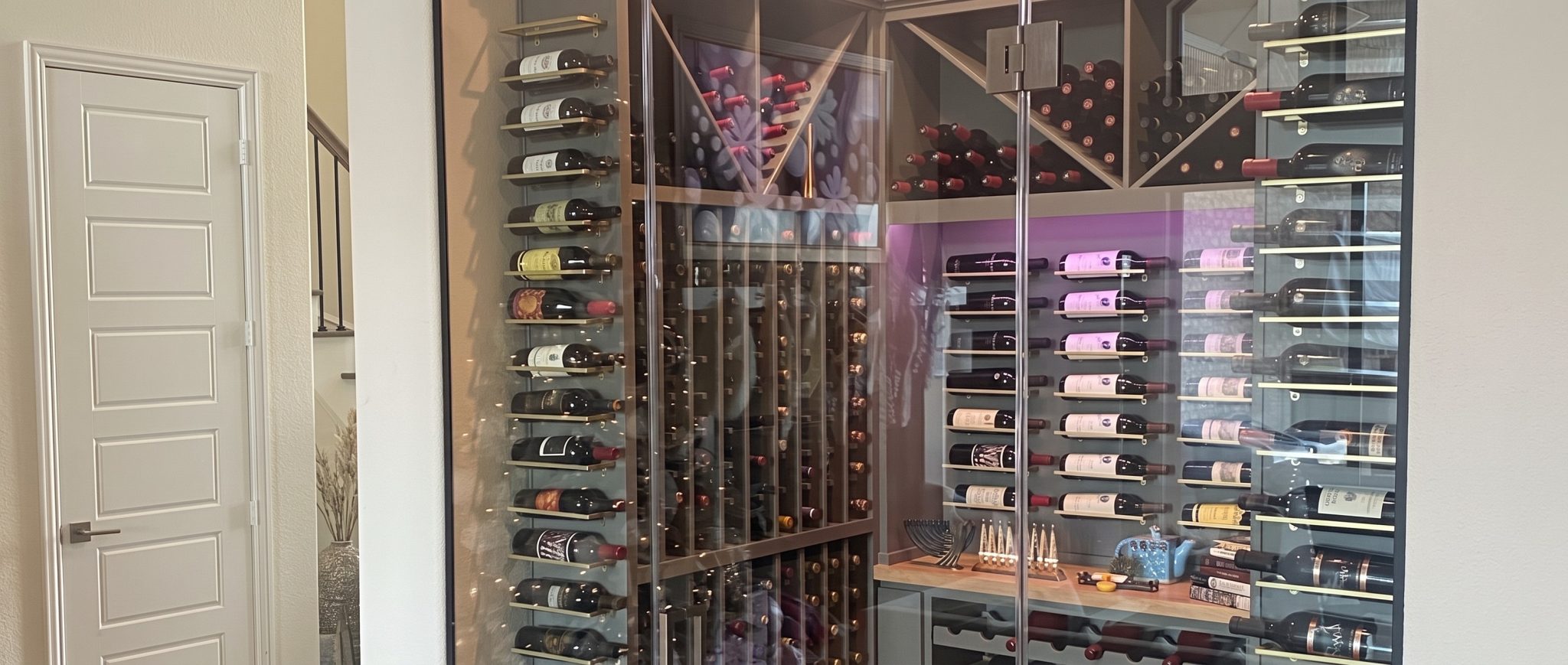 Frameless glass wine room with floor-to-ceiling bottle racks and accent lighting