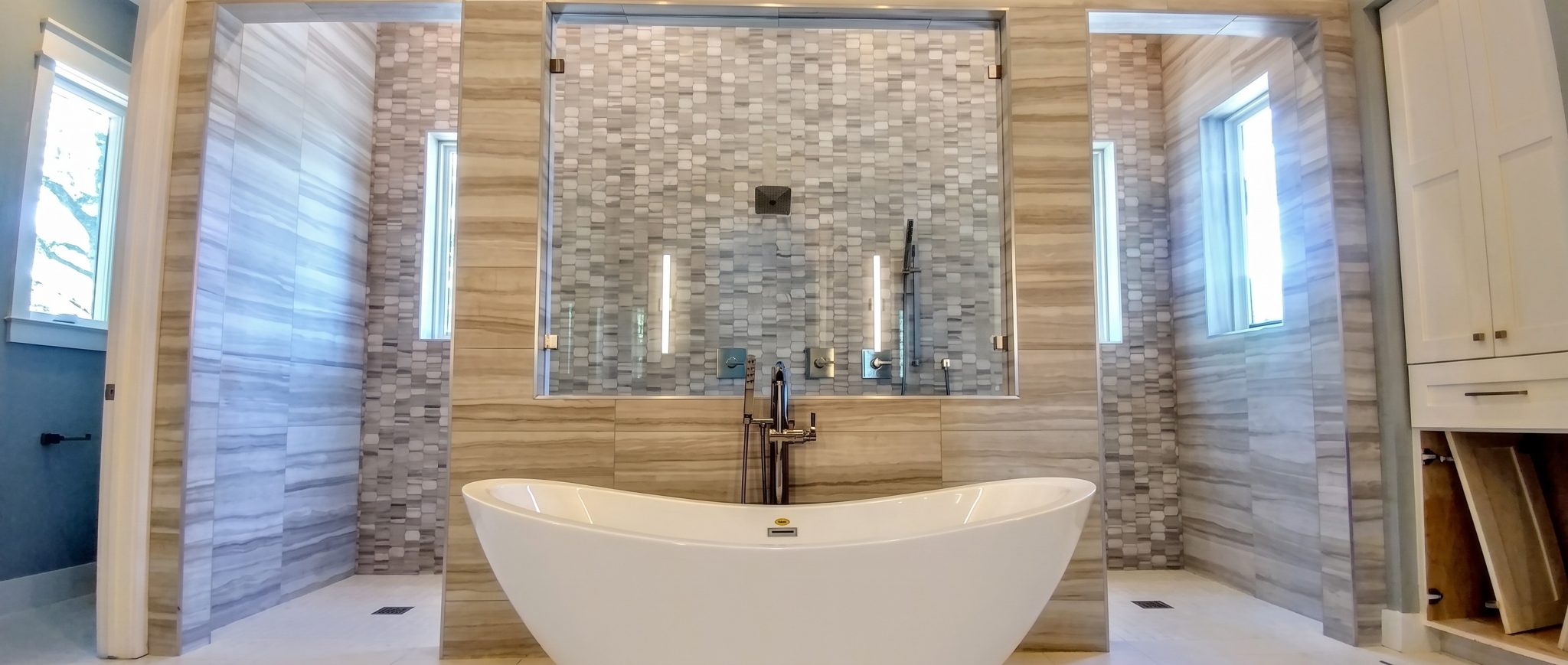 Custom bath with twin frameless walk-in glass showers on either side of a freestanding tub