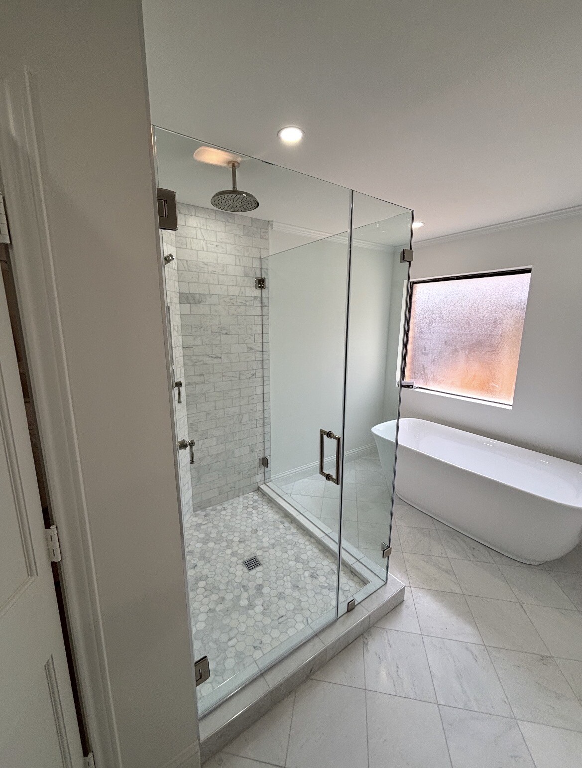 Frameless 90-degree glass shower enclosure with polished nickel hardware beside a freestanding tub in Dallas, TX