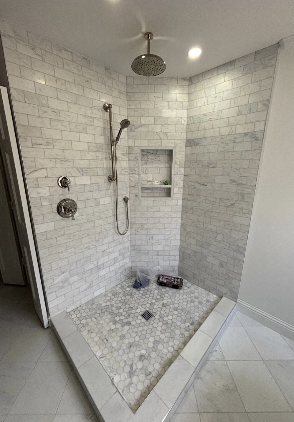 White marble subway tile shower with hexagon floor before the frameless glass enclosure was installed in Dallas, TX