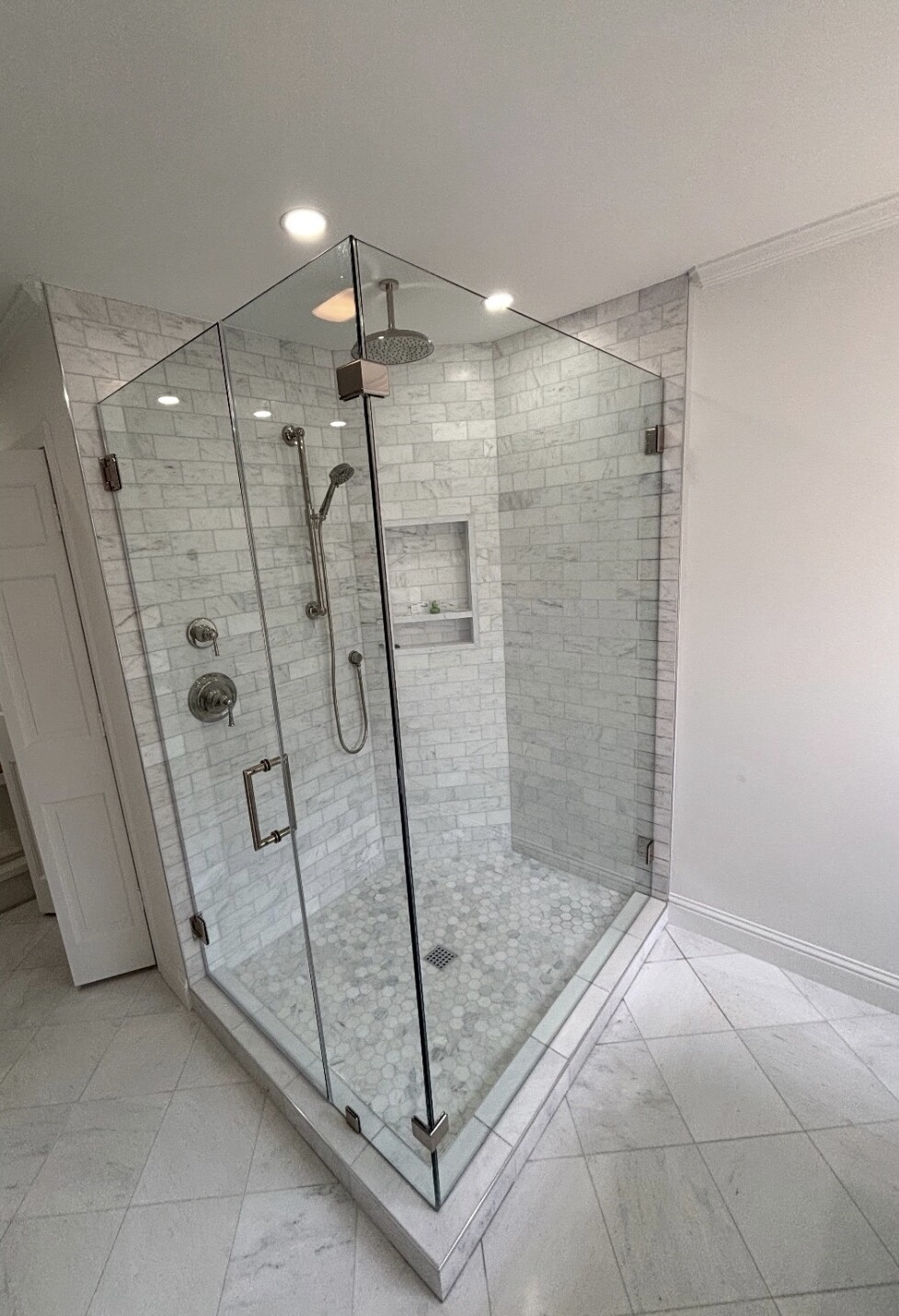 Finished frameless 90-degree shower enclosure with polished nickel hinges and clamps over a hexagon shower floor in Dallas, TX