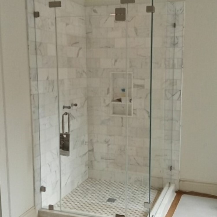 Frameless corner shower enclosure with white marble tile and a chrome door pull