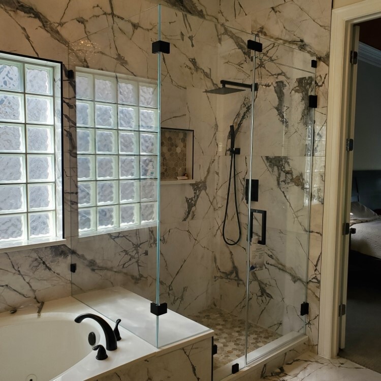 Frameless shower glass beside a glass block window and veined marble tile