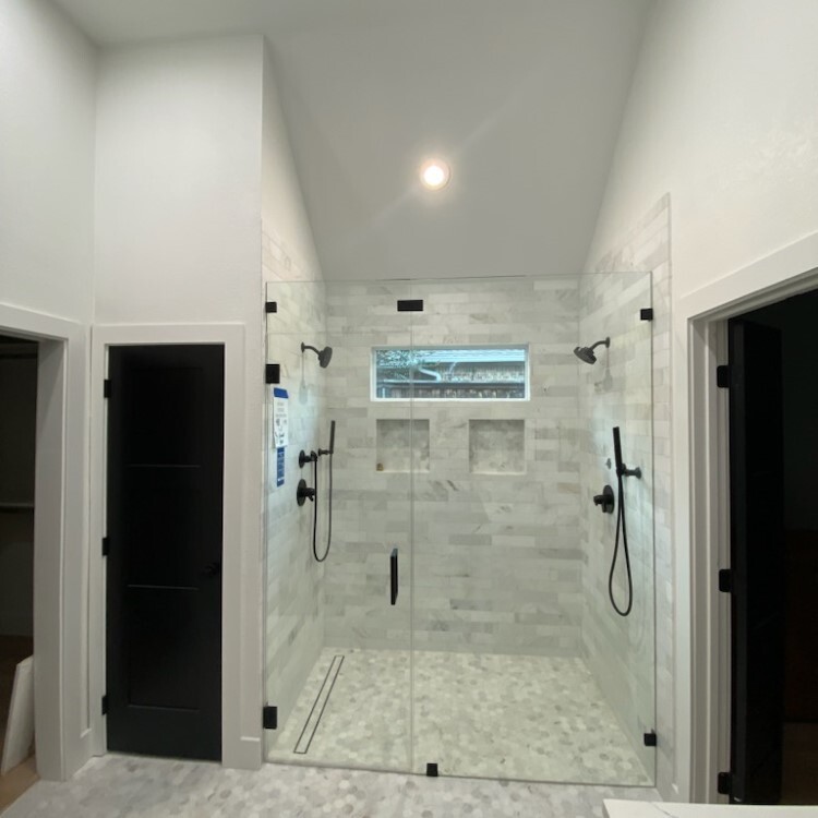 Frameless inline shower enclosure with matte black hardware in a long walk-in shower