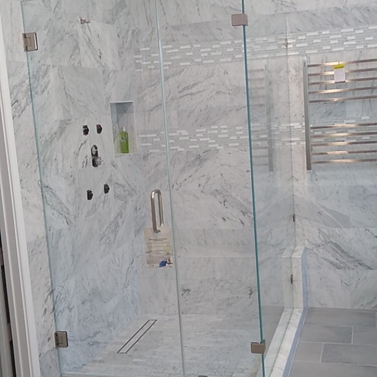 Frameless shower enclosure with white marble tile and a heated towel rack