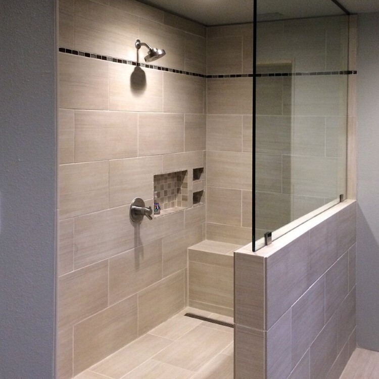 Frameless glass panel on a tiled half wall beside a walk-in shower with a built-in bench