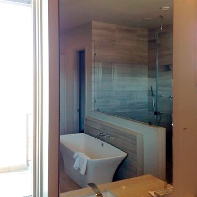 Frameless glass panel on a half wall next to a freestanding tub