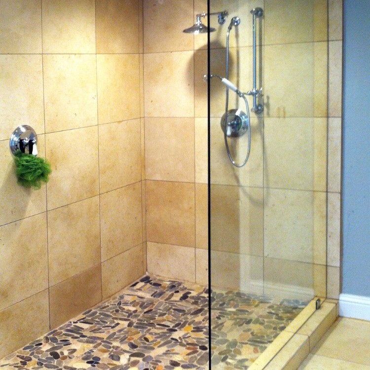 Frameless glass shower panel over a pebble stone floor with travertine tile