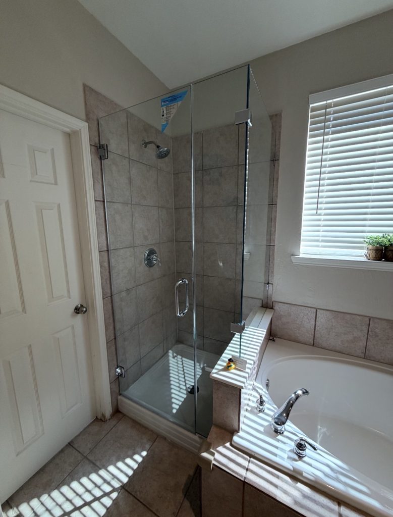 Frameless 90-degree shower enclosure with polished chrome hardware over a pony wall next to a soaking tub in Sachse, TX