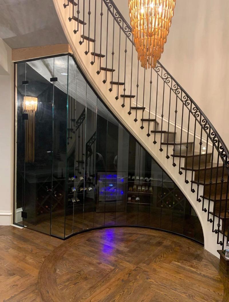 Curved frameless glass wine room built under a sweeping staircase in a Dallas home