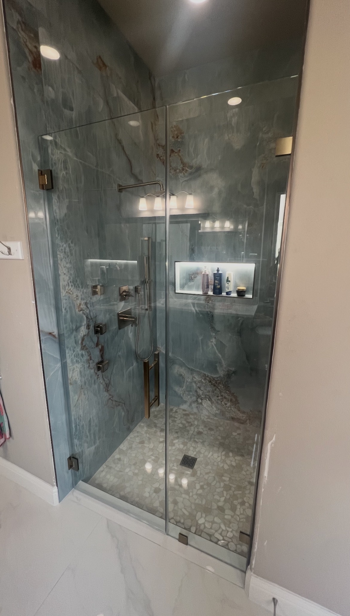 Frameless inline glass shower enclosure with brushed bronze ladder handle in Frisco, TX
